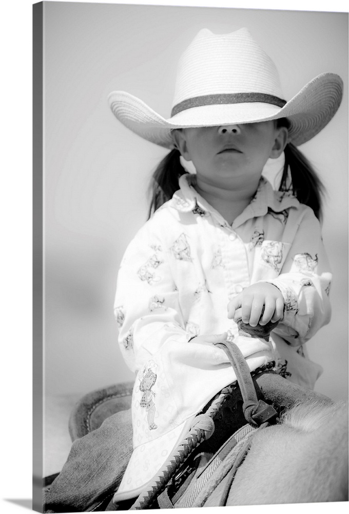 Black and white portrait of a young girl with a cowboy hat covering her eyes on horseback.