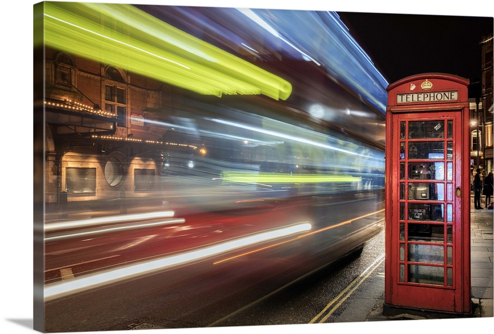 An artistic photograph of telephone booth in London at the edge of a city street with bright neon light trails speeding by.