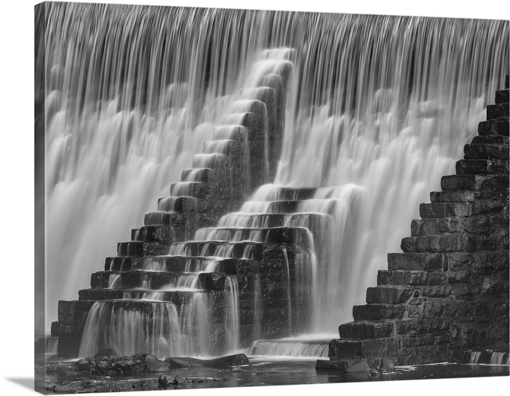 An artistic black and white photograph of staircases leading up to nothing against the veil of a waterfall.