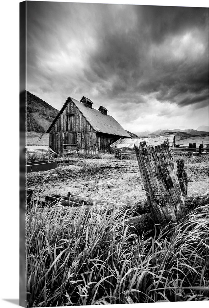 A black and white photograph of a barn and field under a storm clouds.