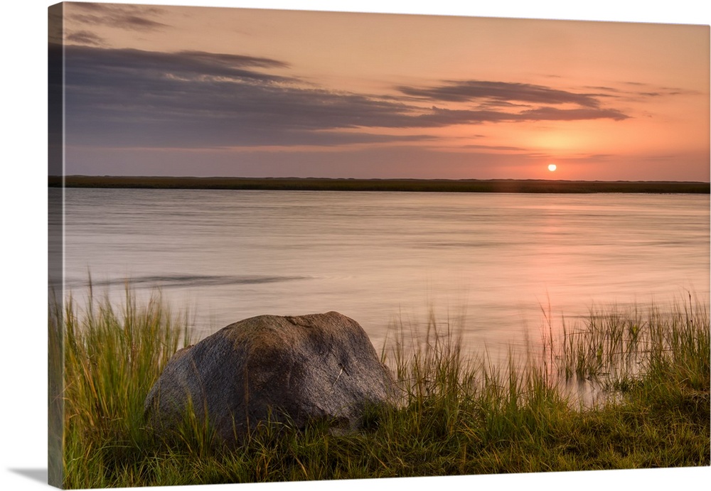 Landscape photograph of a warm sunset over water with a rock in the foreground.