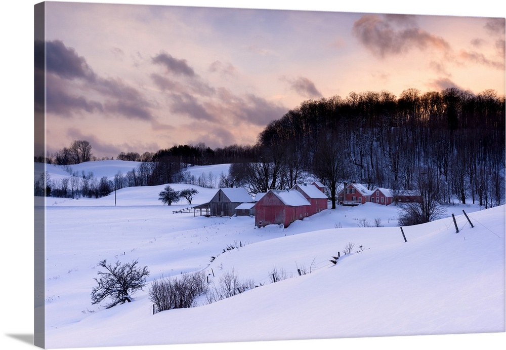 Landscape photograph of a snowy Winter farm with red wooden buildings and a pretty sunset.