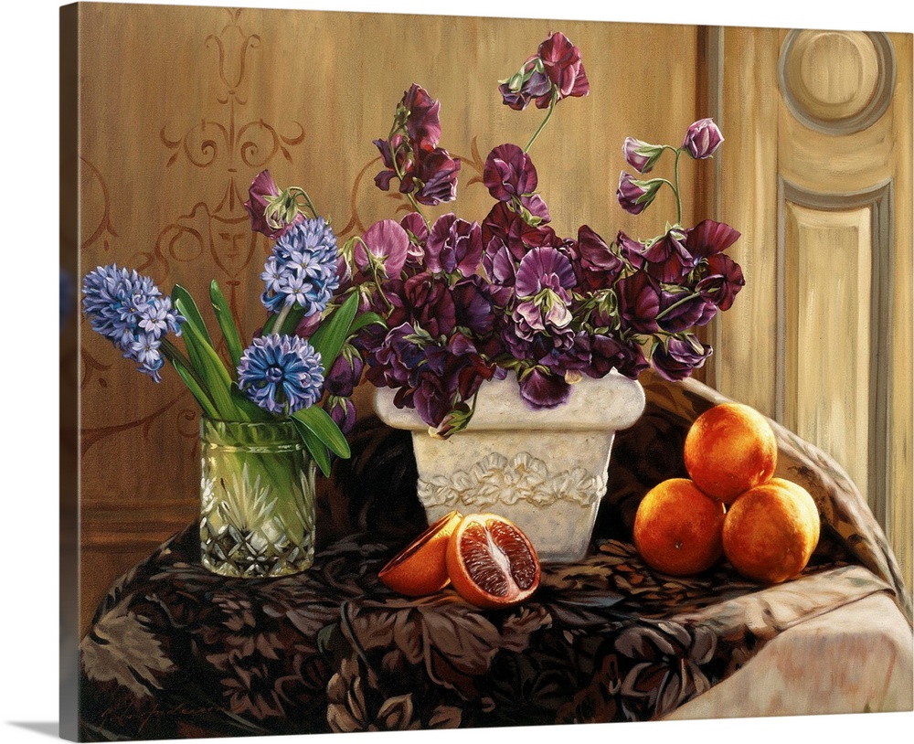 A large white vase filled with purple flowers, one clear vase filled wtih blue flowers and blood oranges on the table.