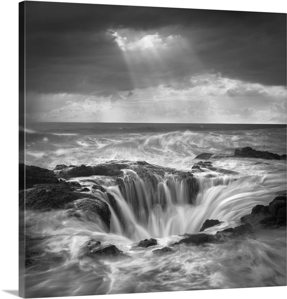 An artistic black and white photograph of a tidal pool with rushing water flowing in and around the rocky edges.