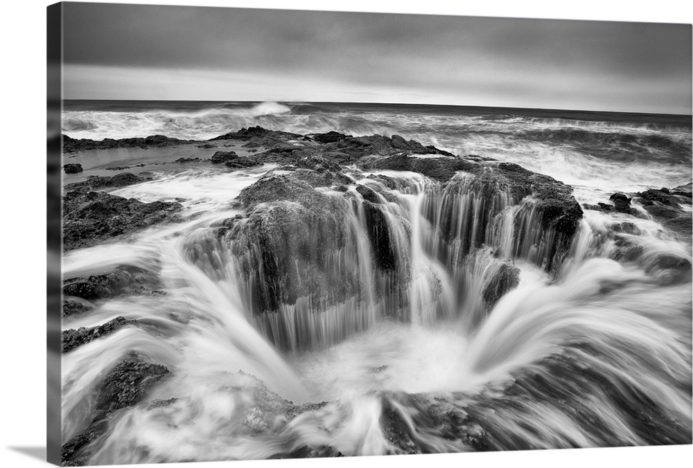 A black and white photograph of a well in the ocean surrounded by rushing water.