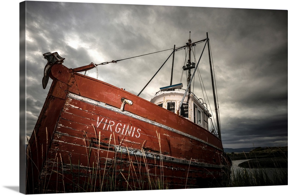 Photograph of an old red boat called "Virginis" pulled up on the shore on a dark overcast day.