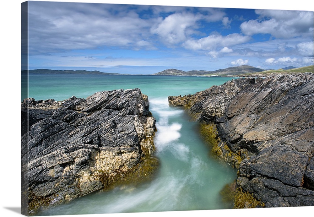 Landscape photograph of crystal blue waters rushing though a gap between rocky cliffs.