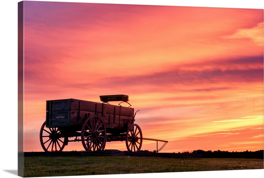 Landscape photograph of a horse drawn, wooden wagon in a field with a stunning warm sunset.