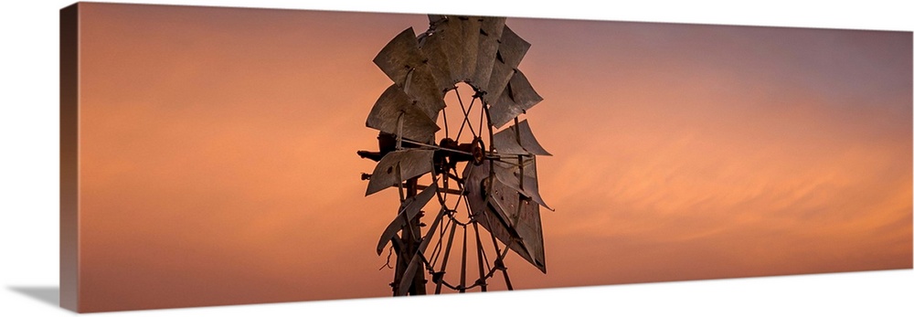 A photograph of a farm windmill under an orange sky.