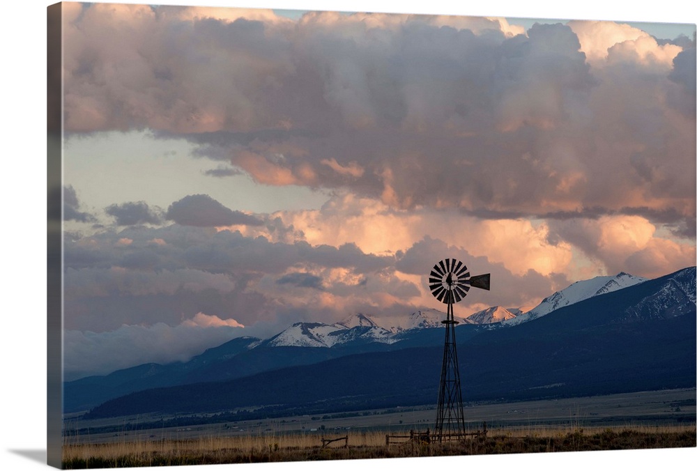 Landscape photograph of a windmill in a field with snow covered mountain peaks in the distance.