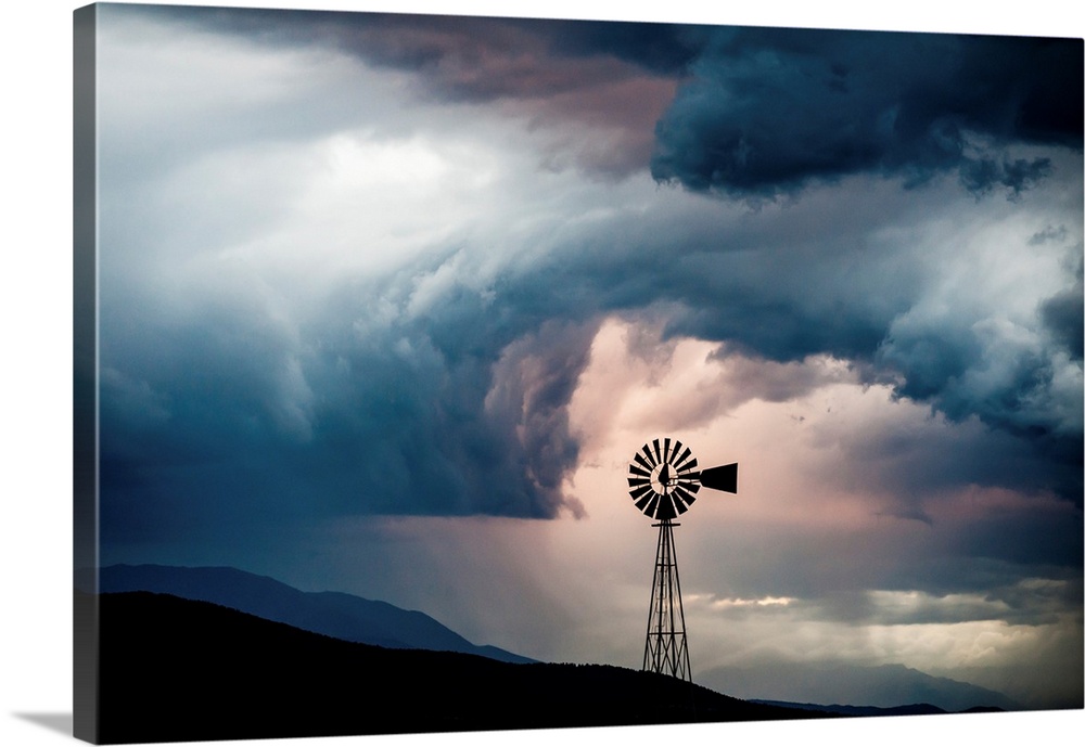 Landscape photograph with a silhouetted windmill amongst rolling hills and a dramatic cloudy sky.
