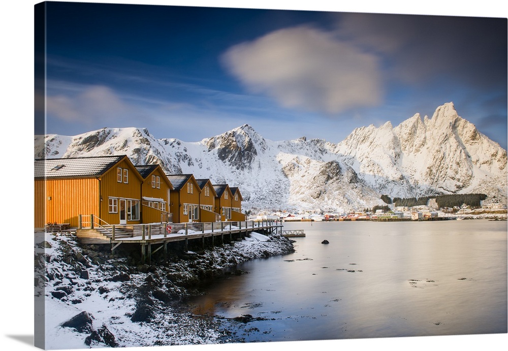 A photograph of a Norwegian yellow cabin village seen with a mountain covered in snow in the background.