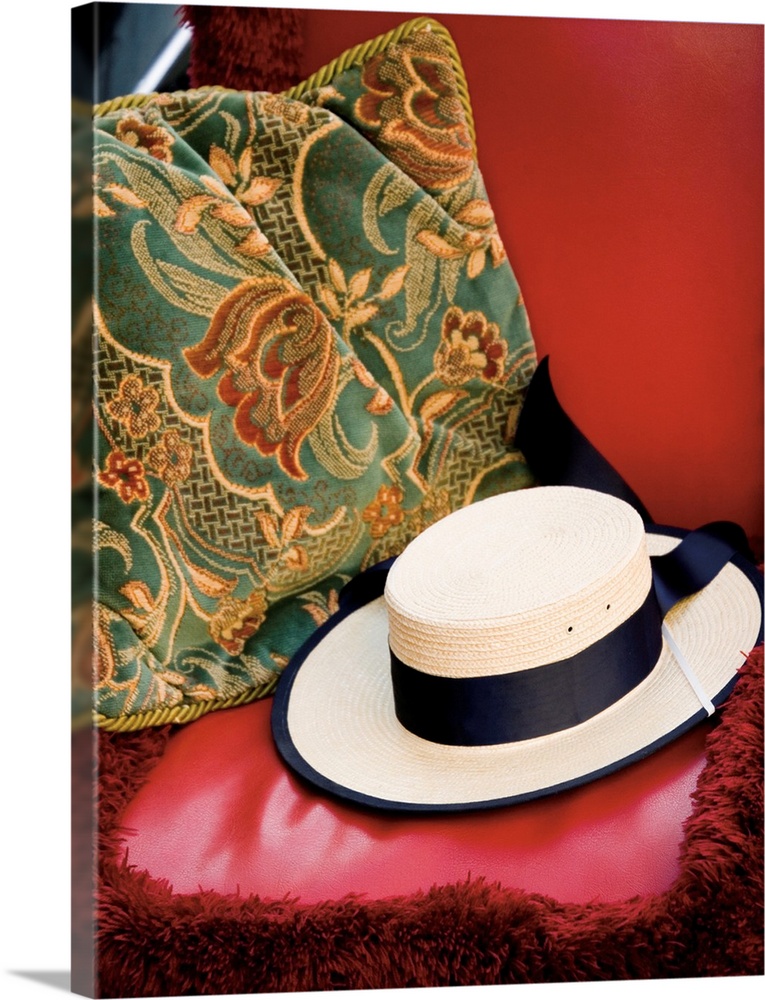 A photograph of a white straw hat sitting on a red leather bench with a floral pillow.