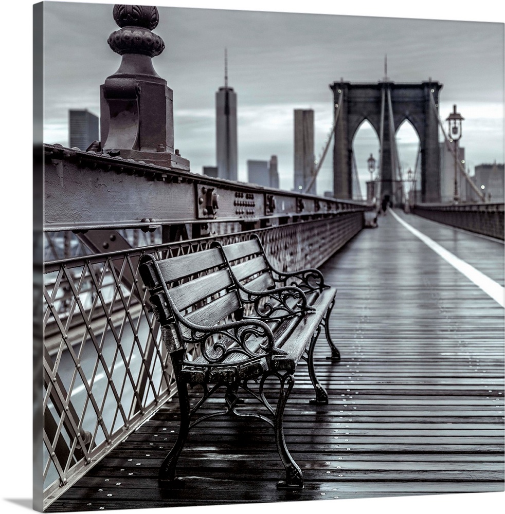 Black and white photograph of a bench on the crosswalk of the Brooklyn Bridge.