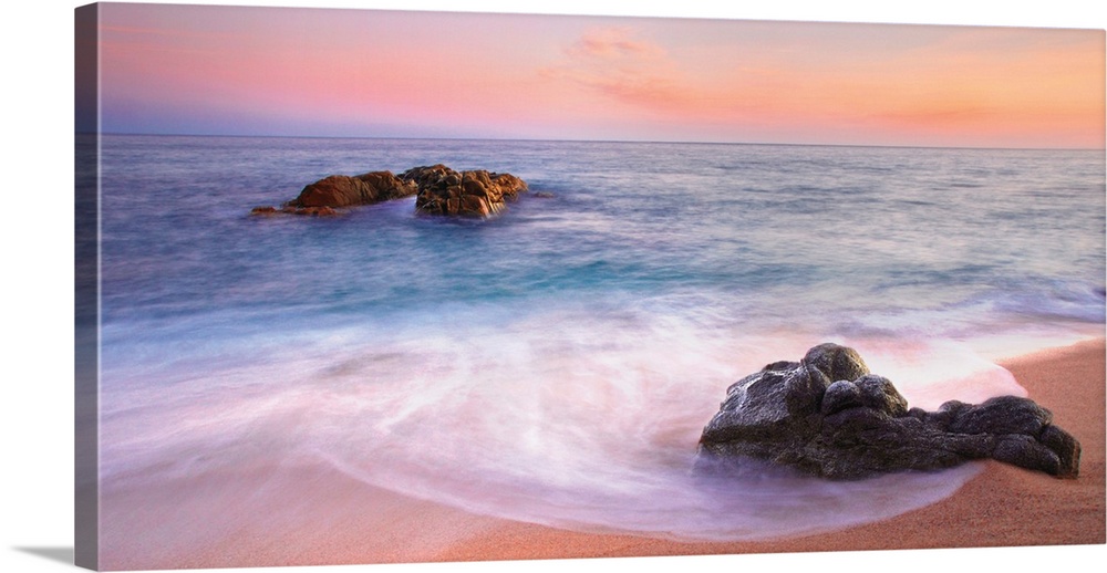 Panoramic image of gentle waves on a rocky seashore with a vibrant pink sunset.