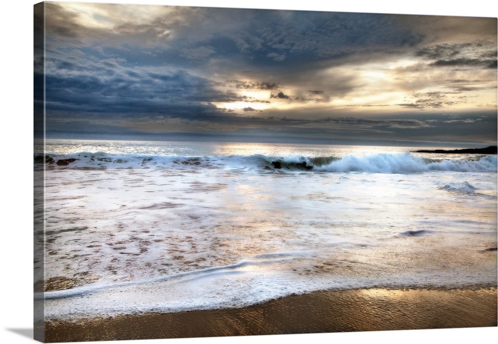 Photograph of foamy waves crashing onto the beach with a stormy sky above.