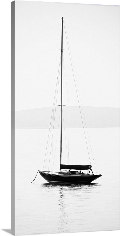 Black and white photograph of a sailboat with its sail down on calm water.