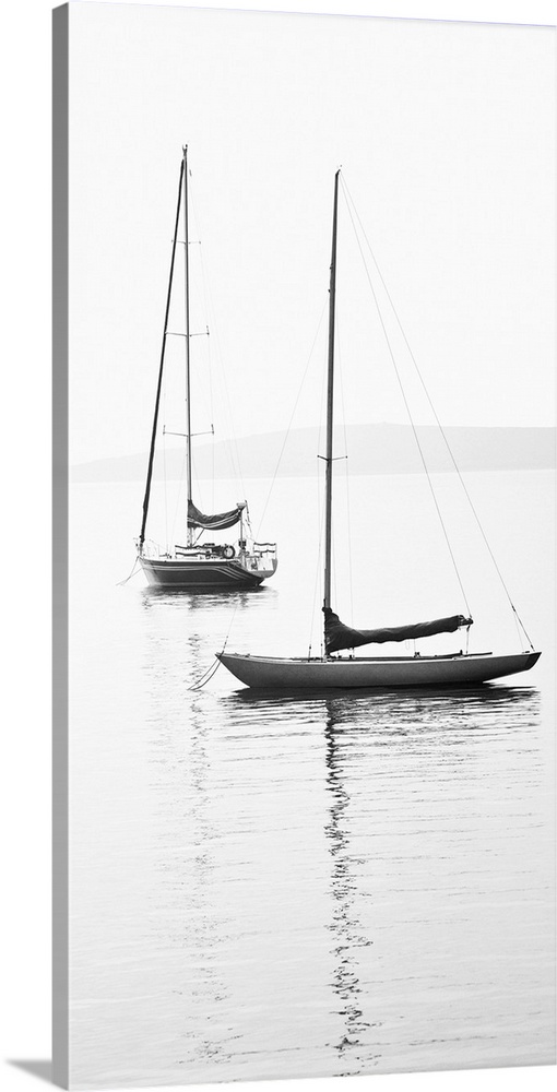 Black and white photograph of two sailboats with sails down on calm water.