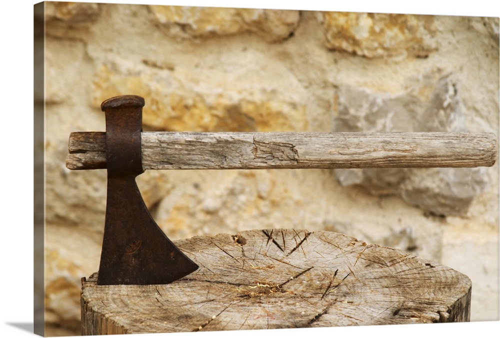 An old rusty ax with a wooden handle struck down in a chopped up piece of wood chopping board.  Moulin Mas des Barres oliv...