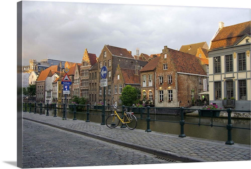Europe, Belgium, Ghent.  A bicycle parked on a paved-stone sidewalk by the water, and historic Ghent architecture.