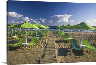 Crete With The City Of Rethimnon With Green Umbrellas And Lounges On The Beach