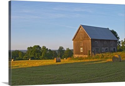 Cut field with hay bales at sunrise. Old farm house barn, Sweden