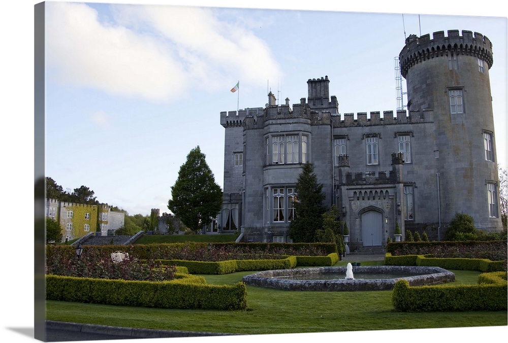 Dromoland Castle Hotel in Newmaket-on-Fergus,Ireland, side view with a fountain,shrubs, lawn and trees under a blue sky wi...