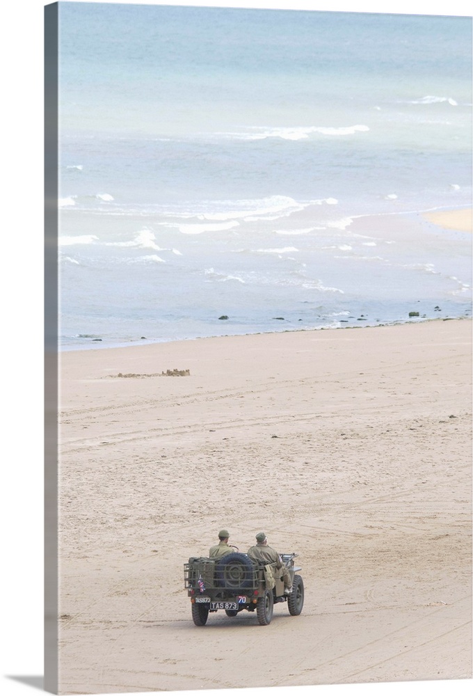 France, Normandy, Saint-Laurent-Sur-Mer, Omaha Beach. Vintage jeep, with soldiers in uniform, driving on historic battlefi...