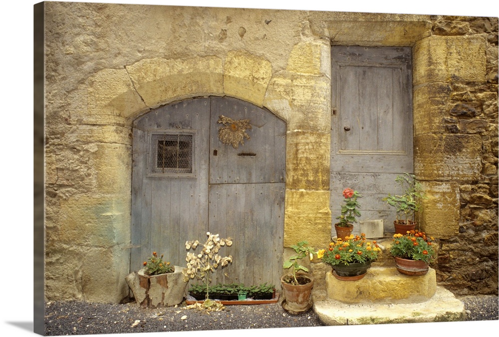 France: St Come d'Oit, stone building with potted plants in front of blue wooden doors, August.