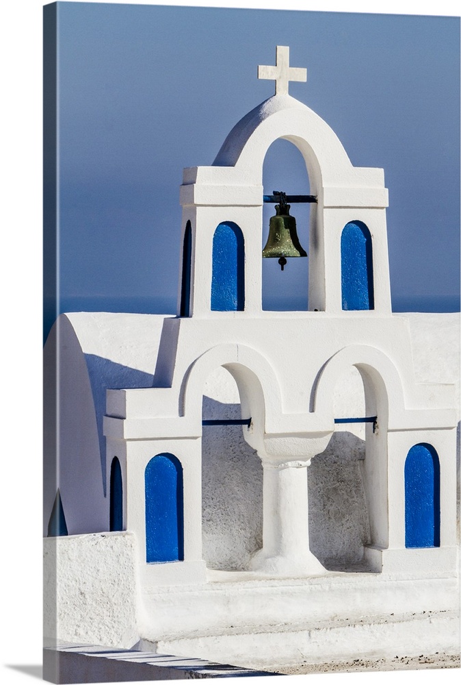 Oia, Greece. Greek Orthdox Church steeple, cross, bell, and blue arches against Aegean Sea.