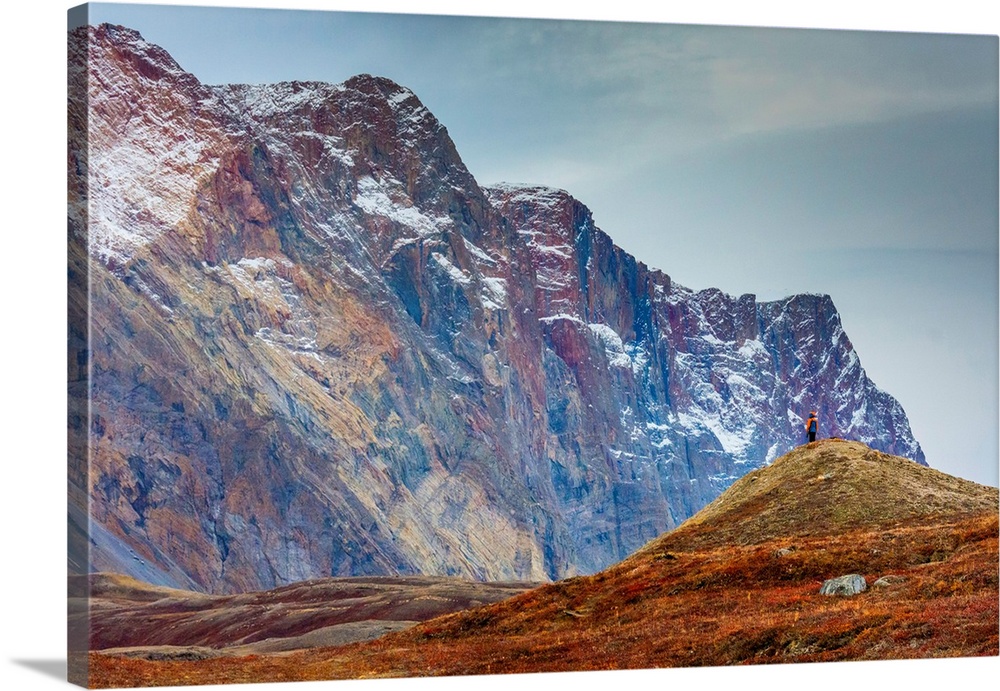 Greenland. Northeast Greenland National Park, Kong Oscar Fjord. Ella Island. Hiker dwarfed by rocky mountains.