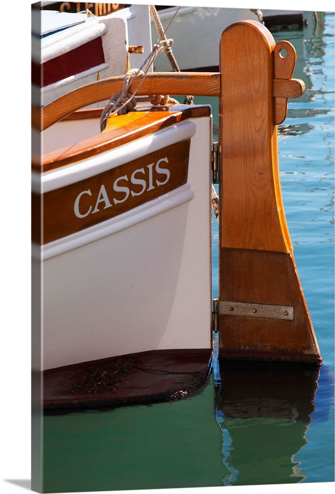 In the harbour in Cassis village.  A traditional style boat with wooden rudder marked with the name Cassis. Painted white....