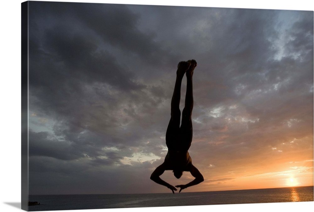 Jamaica, Negril, Silhouette of young man leaping from from cliff above Pirates Cave
