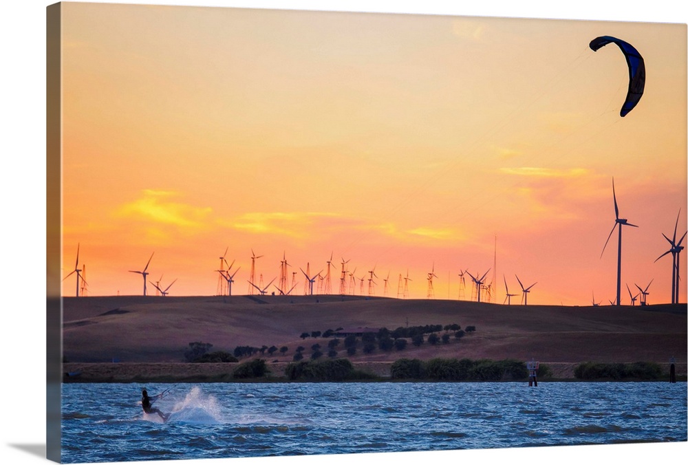 North America, United States, California, Rio Vista, Sacramento River Delta. Kiteboarder at sunset with wind farm turbines...