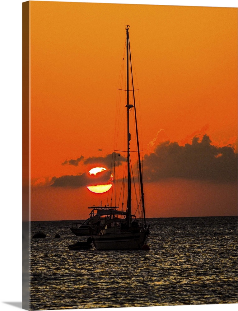Seven Mile Beach, Grand Cayman. Sailboat and a boat with the orange sun setting behind the clouds on the Caribbean Sea