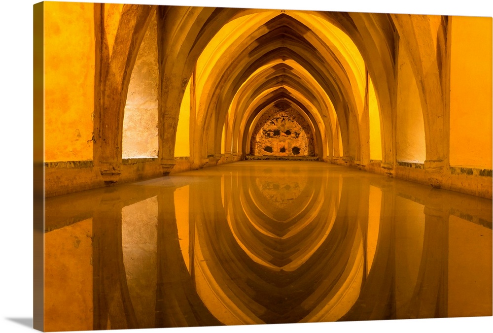 Spain, Andalusia, Seville. The repeating arches of the interior of the baths reflect in the calm water in the Alcazar.