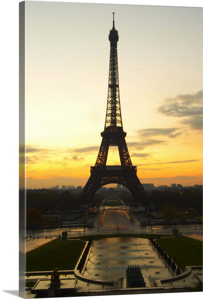The Eiffel Twoer in Paris in early morning dawn with the sun rising on the horizon, pale blue sky some white clouds and th...