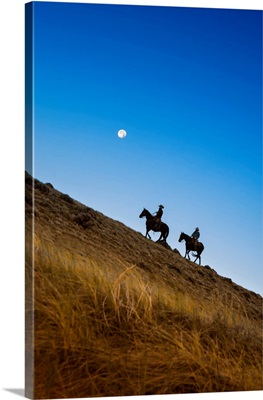 Two Wranglers Riding Horses Up A Hill With Full Moon In Background At Blue Hour