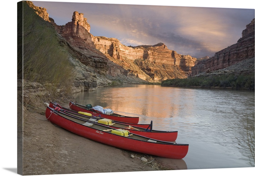 USA, Utah, Canyonlands National Park. Three red canoes rest on bank of Green River.