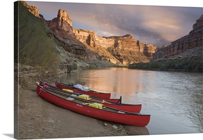 Utah, Canyonlands National Park, three red canoes rest on bank of Green River
