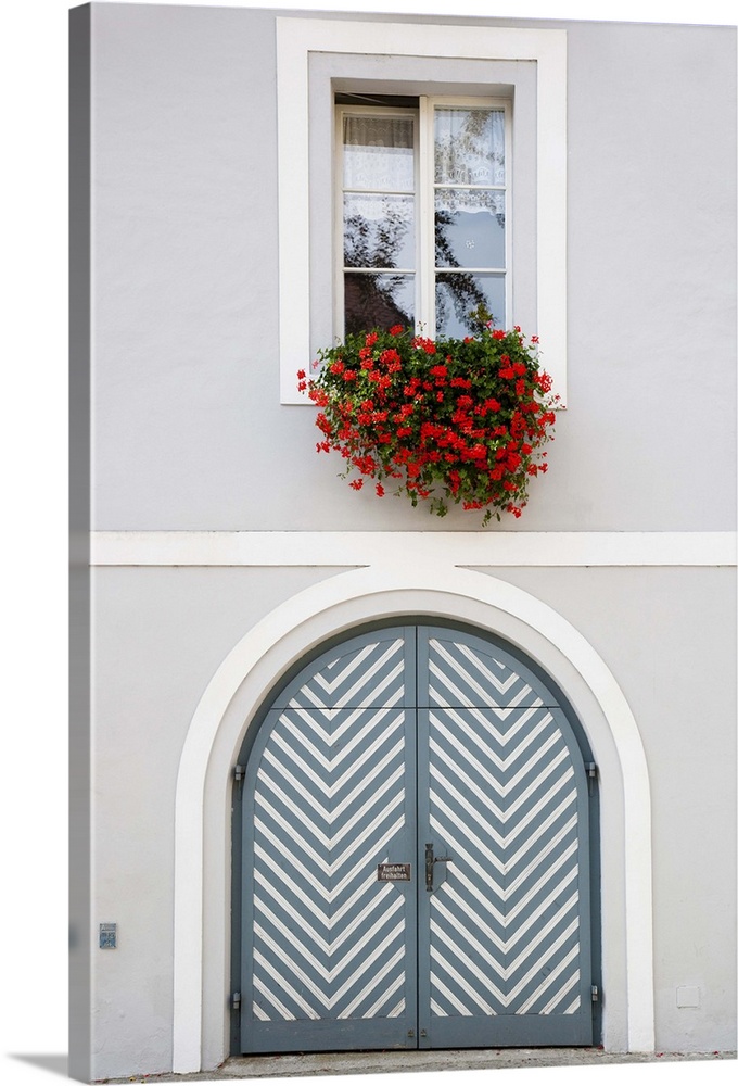 Wels, Upper Austria, Austria - Red flowers are hanging from an open window over a teal door with white stripes. Vertical s...
