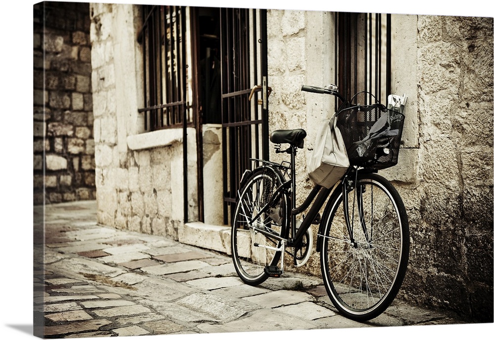 Old bicycle with basket and shopping bag parked in the narrow cobble street.