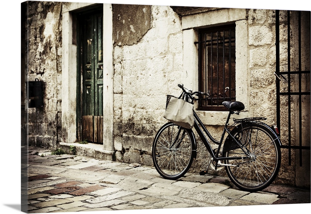 Bicycle with a shopping bag on handle bar, left beside old stone wall.