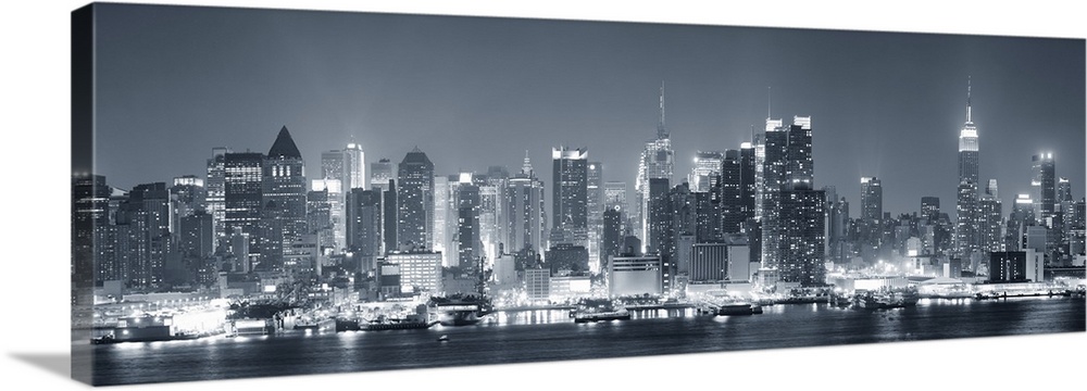 Manhattan midtown skyline in black and white at night with skyscrapers lit over Hudson River with reflections.