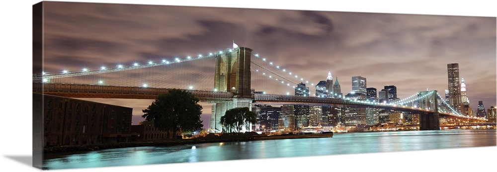 Panoramic view of Manhattan with Brooklyn Bridge at night with skyscrapers illuminated over the Hudson River.
