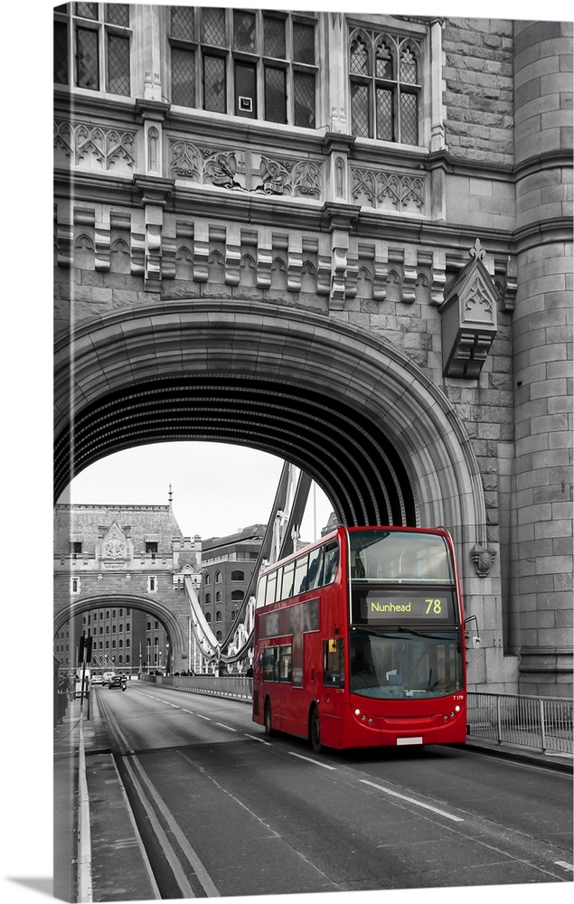 Red London bus passing over Tower Bridge in black and white with selective color.