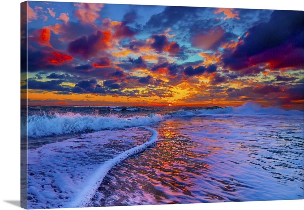 Ocean waves break onto the beach under a pink, blue, and purple puffy cloud sunset.