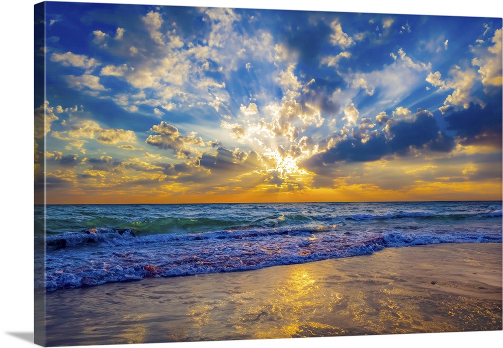 Sunrays at sunset break through the blue sky and cast golden sunlight onto the beach.