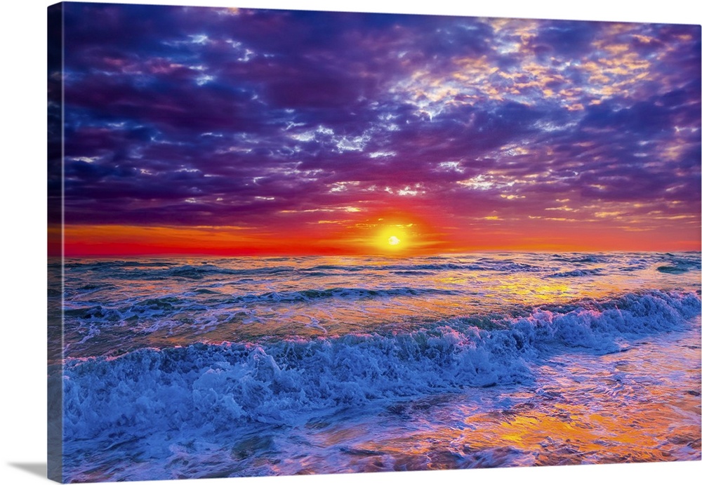 Blue ocean waves crash onto the beach beneath a red, lavender, and purple sunset.