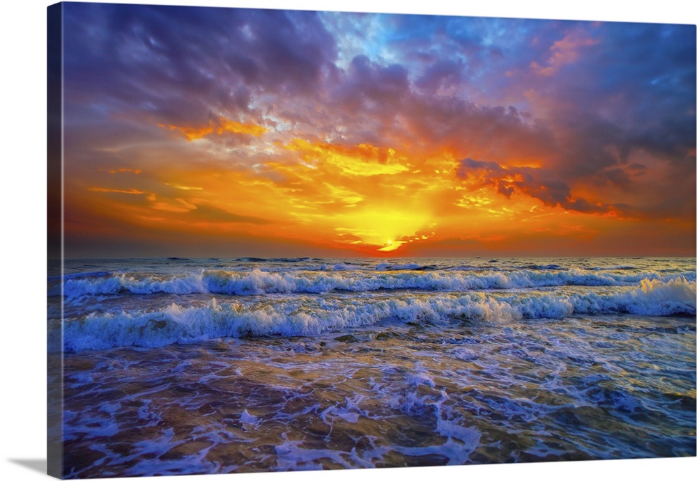 Purple and blue clouds hover above a brilliant red and orange sunset. A cold blue ocean with sunset illuminated breaking w...